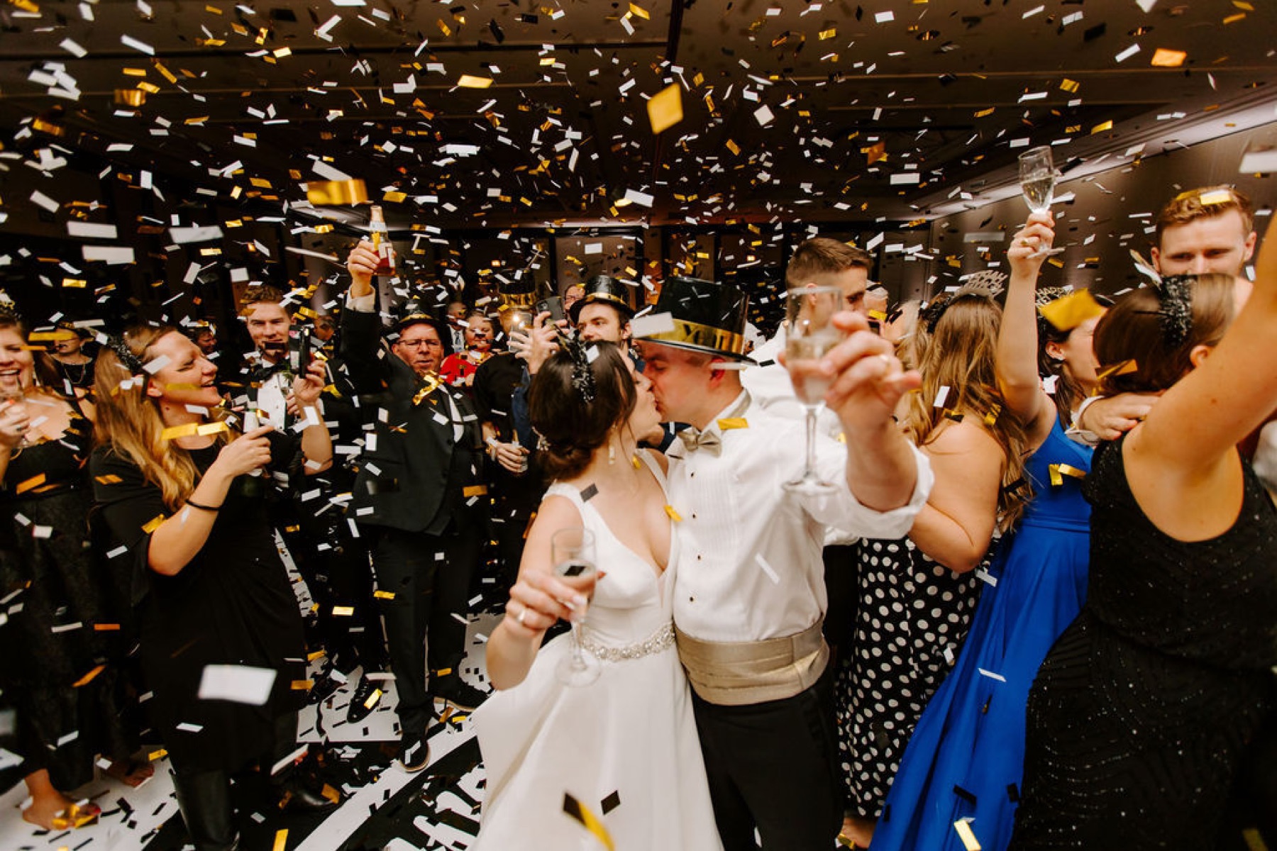Newlyweds kissing under falling confetti on a crowded dance floor